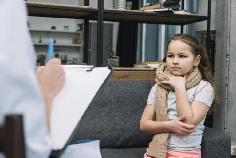 SICK GIRL WITH SCARF AROUND HER NECK SITTING FRONT WOMAN WRITING CLIPBOARD WITH PEN